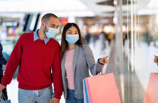milenario multirracial Pareja en cara mascaras compras a supermercado, señalando a Tienda ventana, elegir bienes. joven diverso familia con regalo pantalones comprando cosas a centro comercial durante coronavirus pandemia foto