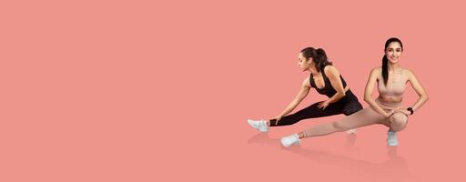 Two women are engaged in stretching exercises on a bright pink background. They demonstrate flexibility and strength while wearing activewear. The atmosphere is energetic and motivating. photo