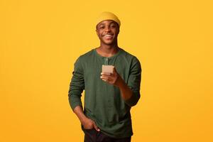 Online Communication. Portrait of cheerful young black man holding smartphone and smiling at camera, happy millennial african guy using cellphone while standing over yellow background, copy space photo