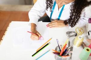 Middle aged woman works attentively at her office desk, sketching designs with colored pencils. Tools and materials are organized around her, showcasing her creative process. photo