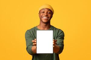 Joyful Black Hipster Guy Demonstrating Digital Tablet With White Blank Screen, Cheerful African American Man Recommending New App Or Website While Standing Isolated Over Yellow Background, Copy Space photo