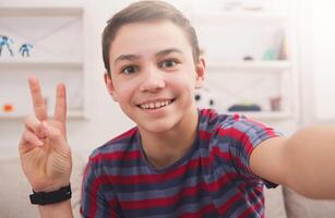 Happy teenager making selfie for social networks. Boy at home on sofa in living room photo