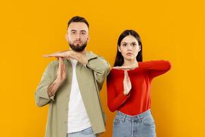 A young Caucasian couple stands together, playfully using hand signals to convey affection. Their vibrant expressions reflect a strong bond, set against a bold, bright yellow backdrop. photo