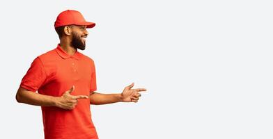African Courier Guy Pointing Fingers Aside At Free Space Recommending Delivery Service Posing Over Yellow Studio Background. Panorama photo