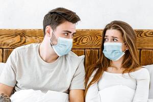 Disease and quarantine concept. Sad guy and girl in protective masks are sitting in bed and looking at each other photo