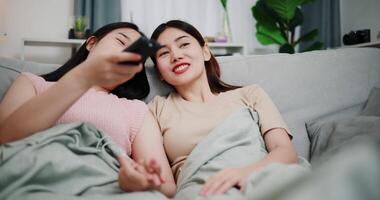 Handheld low angle view shot, Asian lesbian couple happily chatting while watching television together in a cozy room at home. A moment of love and happiness. LGBTQ lifestyle. video
