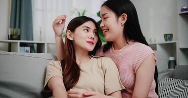 Handheld low angle view shot, Asian lesbian couple sit on the sofa, talk and hug happily, sharing good feelings with each other in the living room at home. LGBTQ Lifestyle. video