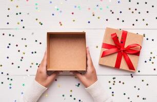 Christmas presents delivery service. Female hands with empty open gift box on white wooden background, top view, copy space photo