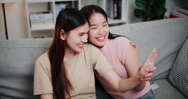 Handheld high angle view shot, Asian lesbian couple sitting on sofa happily admiring their engagement rings in a romantic atmosphere in a cozy room at home. LGBTQ Lifestyle. video