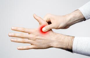 Inflammation in muscles and joints. Man holds to highlighted red hand isolated on gray background, studio shot photo