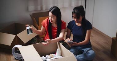 Handheld high angle view shot, Two siblings happily chatting on the floor and using mobile phone to check if the items in the boxes they moved from old house are complete. Moving to a new home concept video