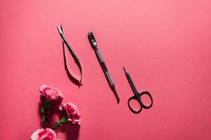 A selection of manicure tools, including scissors and cuticle pushers, is arranged on a vibrant pink surface alongside fresh flowers, highlighting a pampering service at a nail salon. photo