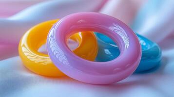 Three vibrant plastic rings in yellow, pink, and blue sit atop a soft fabric. The natural light enhances the glossy texture and vivid colors, creating a playful atmosphere. photo