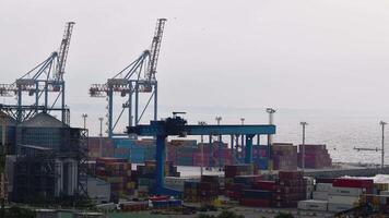Container port terminal at shoreline with seasurf waves. Silhouettes of huge bridge cranes with raised jibs. Time lapse of loading machinery and container stack in sea port Odessa, Ukraine, 09 29 2020 video