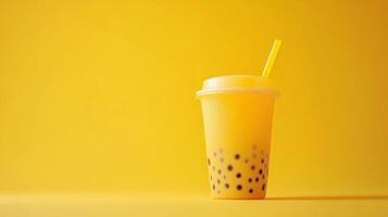 A vibrant cup of yellow bubble tea filled with tapioca pearls stands against a matching solid background. The drink features a straw and offers a refreshing visual appeal. photo