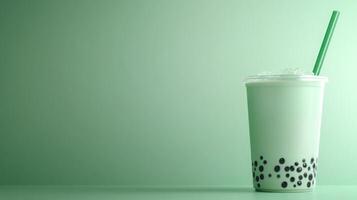 A clear cup filled with green bubble tea showcases black tapioca pearls at the bottom. The drink is topped with ice and has a green straw, creating a refreshing look in soft pastel tones. photo