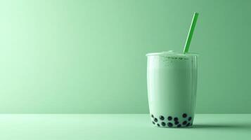 A clear glass filled with a green beverage and topped with a green straw sits on a smooth surface. The drink contains tapioca pearls at the bottom, offering a unique texture and flavor. photo