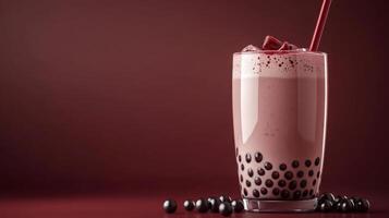 A tall glass of pink bubble tea with tapioca pearls and a red straw sits on a red table. A few tapioca pearls have spilled out of the glass and are scattered on the table. photo