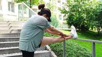 Young woman in sportswear is doing exercise in city park. Warm up before running or jogging. Outdoor sports training concept. High quality 4k footage video