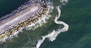 sea waves against the rocks of a breakwaters port, aerial overhead with drone video
