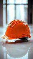Bright orange hard hat resting on a table in an industrial workspace with large windows photo