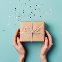 Gift wrapped in brown paper with twine on a blue background with silver confetti scattered photo