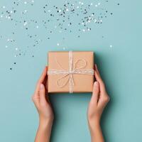 Gift wrapped in brown paper with twine on a blue background with silver confetti scattered photo