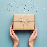 Gift wrapped in brown paper with twine on a blue background with silver confetti scattered photo