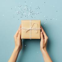 Gift wrapped in brown paper with twine on a blue background with silver confetti scattered photo