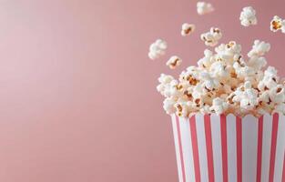 Freshly popped popcorn overflowing from a striped container on a pink background photo