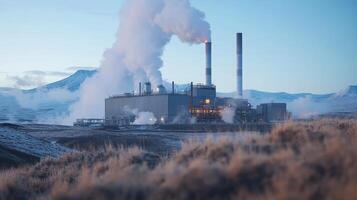 Industrial facility emitting steam, set against a mountainous landscape in a cold environment. photo