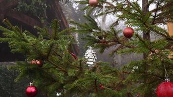Baubles hanging at Christmas tree branches swaying by wind in foggy weather. Rain instead of snowing in winter due to climate change and global warming. Christmas ornaments on xmas tree under drizzle video