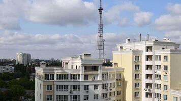 Cumulus clouds move fast from left to right over city buildings and communication tower antenna in residential district of European city. Day timelapse with top of modern yellow building on foreground video