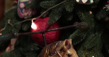 Selective focus artificial Christmas tree decorated with retro Christmas ornaments and lamp garland. Vintage stuffed toy clown with porcelain face on Christmas tree top. Camera moves from down to top video