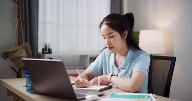Footage of handheld, Female freelancer sitting at desk taking notes on notebook while working on laptop in home office. Working from home, Remote working. video