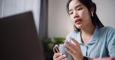 Handheld low angle view shot, Female freelancer holding coffee cup while explaining project in online meeting with team members via laptop in home office. Working from home, Remote working. video