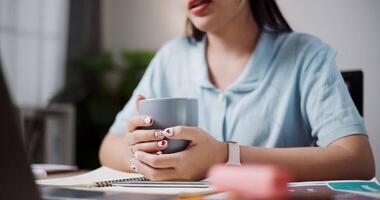 Handheld selective focus shot, Hands of Female freelancer holding coffee cup while explaining project in online meeting with team members via laptop in home office. Working from home, Remote working. video
