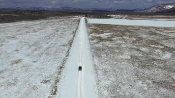 View from a drone on a winter road in a field along which a car is driving video
