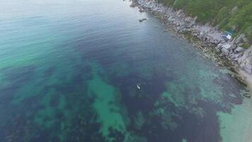 Drone shot along the rocky coast with a man on the sup on a sunny day. video