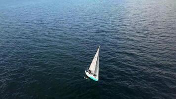 View from a drone of a yacht with white sails on the open sea at sunset video