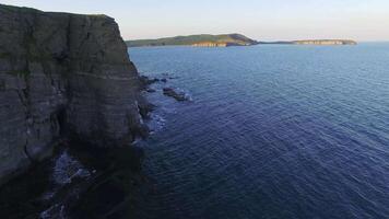 Aerial. Spectacular aerial view of rocky promontory jutting into sea at sunset video