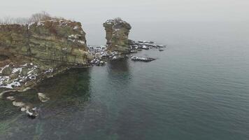 View from a drone on a snow-covered rocky seashore at sunset video