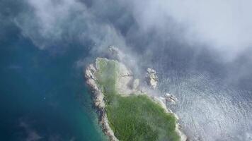 View from drone flying upward the rocky cape on a sunny day shrouded in fog. video