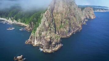 Drone view along the rocky coast and high cliffs on a sunny day shrouded in fog. video