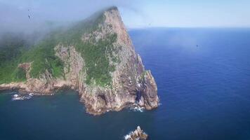 Drone view along the rocky coast and high cliffs on a sunny day shrouded in fog. video