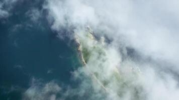 Drone view descending to a rocky promontory on a sunny day shrouded in fog. video