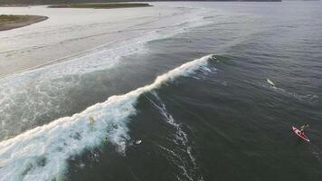 View from a drone to a SUP surfer riding a wave in the sea at sunset video