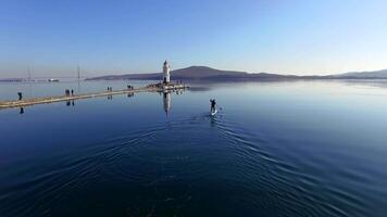 Drone view as a guy in wetsuits row on a sup along the spit with lighthouse video