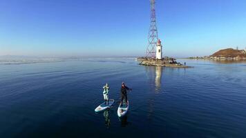 Drone view as a guy and girl in wetsuits row on a sup along the lighthouse video