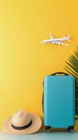 A turquoise suitcase stands beside a wide brimmed straw hat against a vibrant yellow wall photo